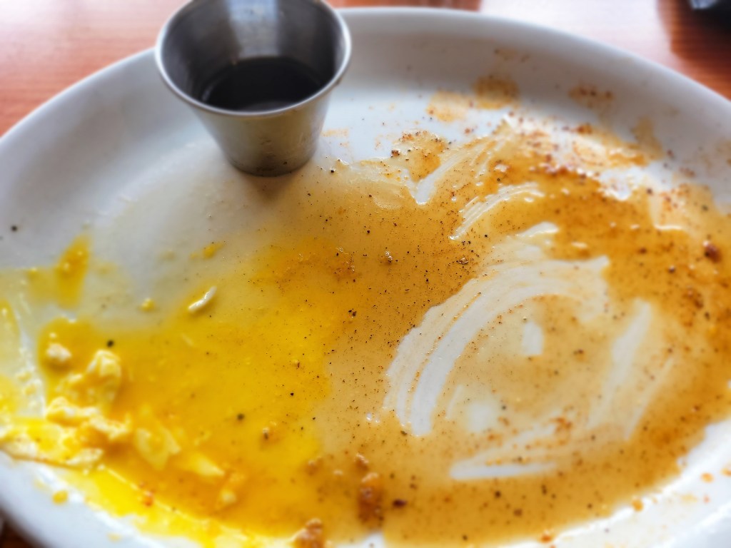 overhead view of white plate with egg yolk and maple syrup after breakfast